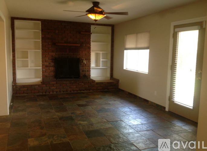 A living room with a brick fireplace and a ceiling fan.