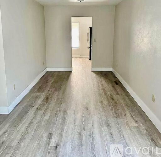 A room with wooden flooring and white walls, with a door at the end.