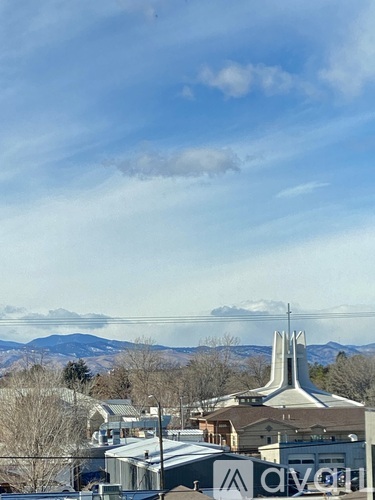 A church with a tall steeple stands out against a backdrop of mountains and a blue sky.