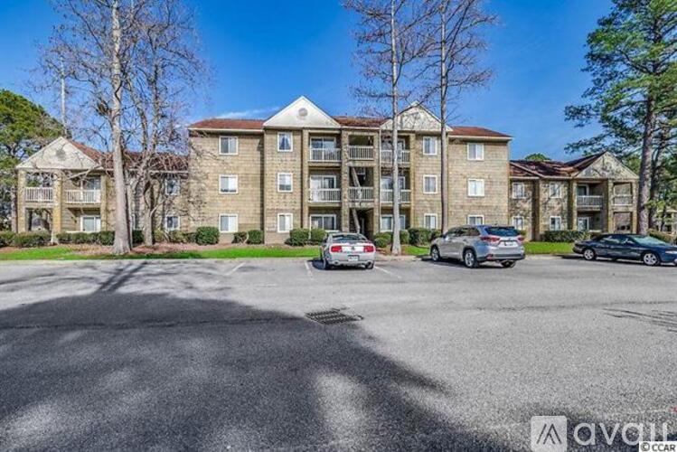 A parking lot in front of a large apartment building with cars parked.