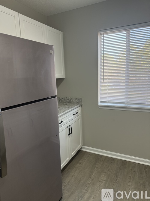 A kitchen with a refrigerator, cabinets, and a window with blinds.
