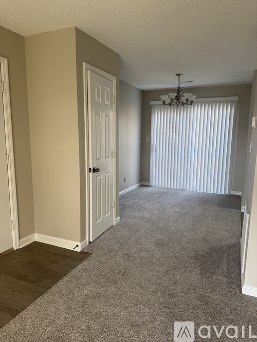 A room with a carpeted floor, a door, and a chandelier.