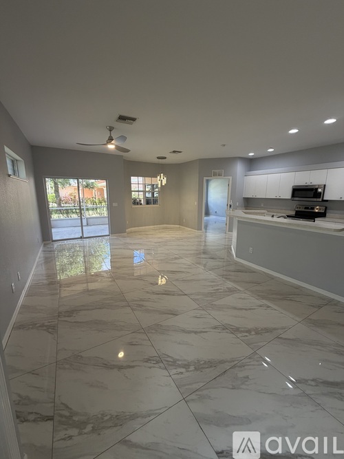 A spacious kitchen and living room with marble flooring and a ceiling fan.