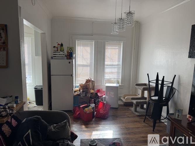 A living room with a lot of clutter and a refrigerator in the corner.