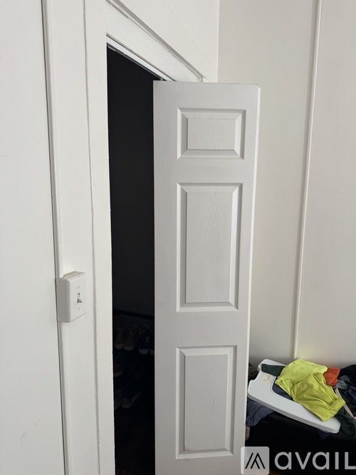 A white door with a handle on the left side and a white shelf with clothes on it.