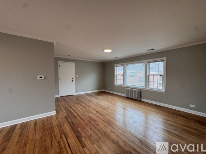 A room with wooden flooring and a window with a view of a building outside.