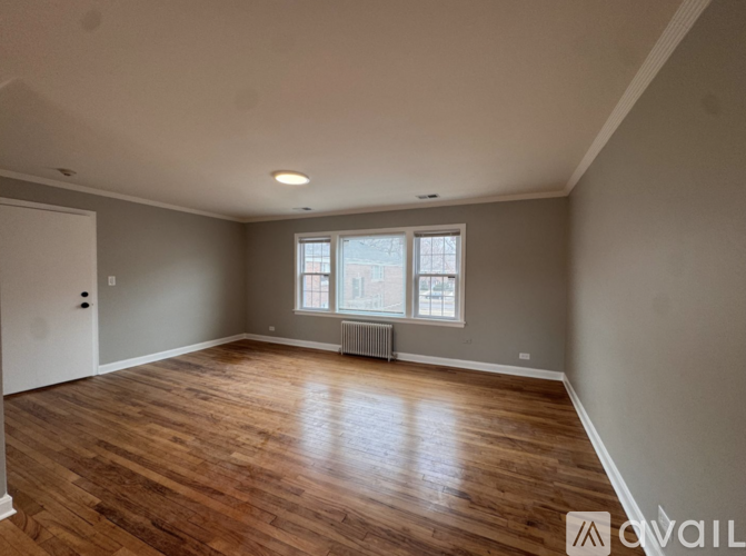 A spacious room with wooden floors and a window with a radiator.