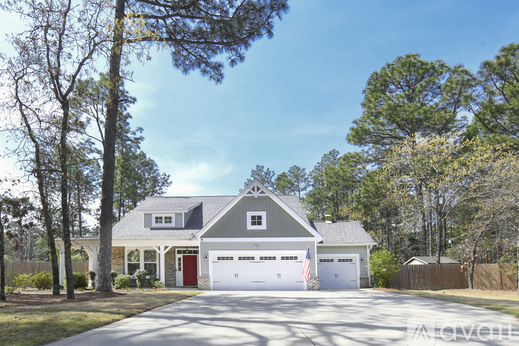 A house with a red door and a garage is surrounded by trees.
