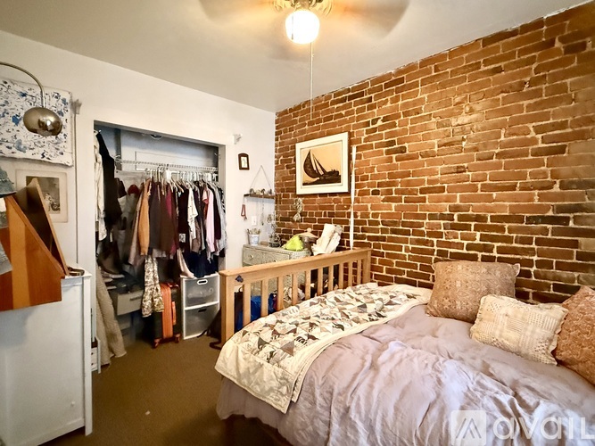 A bedroom with a brick wall and a bed with a white comforter.