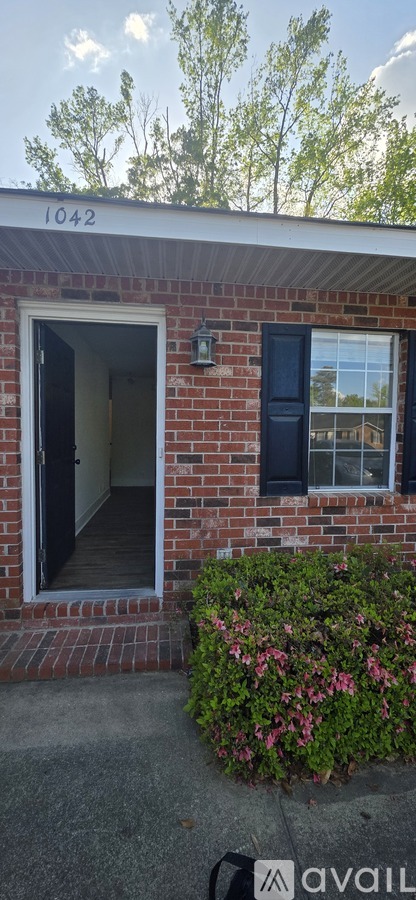 A house numbered 1042 with a blue window and a bush with pink flowers.