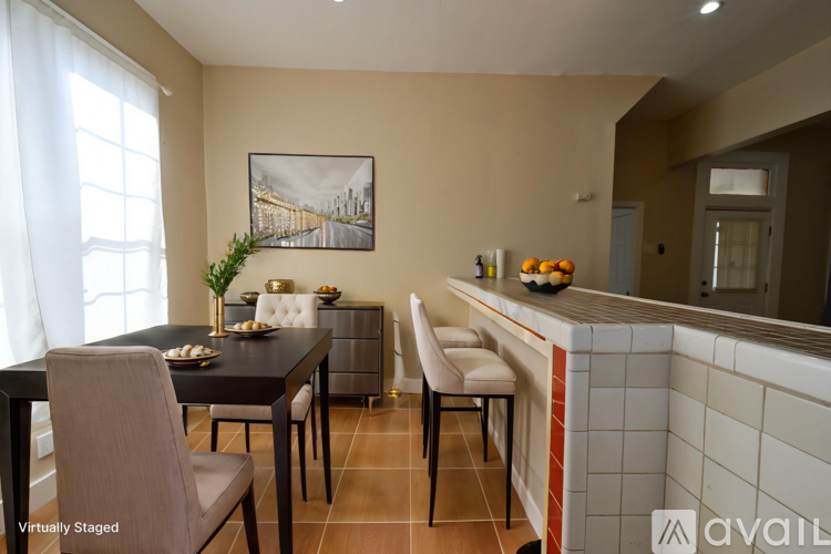 A dining room with a black table and chairs, a framed picture on the wall, and a counter with a bowl of fruit on it.