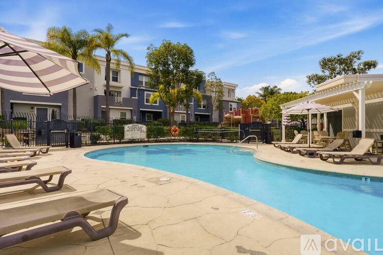 A pool surrounded by lounge chairs and umbrellas in front of a building.