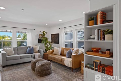 A living room with a grey sofa, a wooden coffee table, a beige armchair, and a bookshelf with various items.