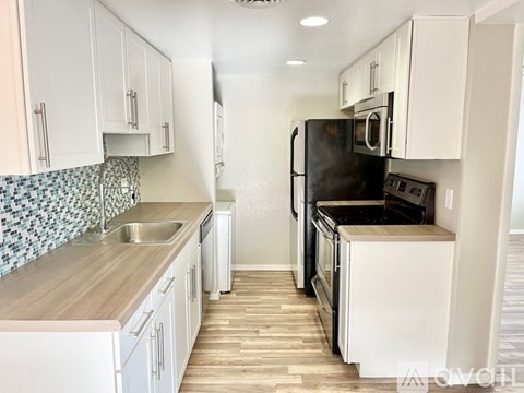 A kitchen with white cabinets and a black refrigerator.