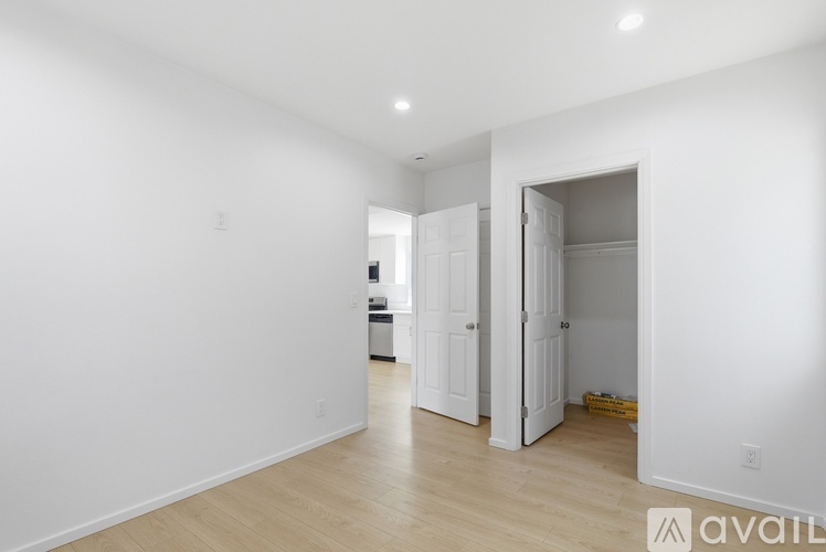 A room with white walls and wooden flooring, with a doorway leading to another room.