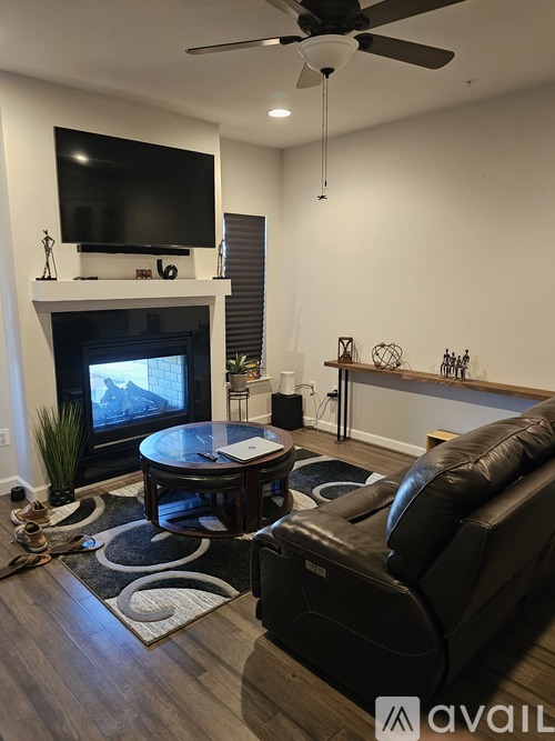 A living room with a black leather couch, a coffee table, a fireplace, and a television mounted above it.