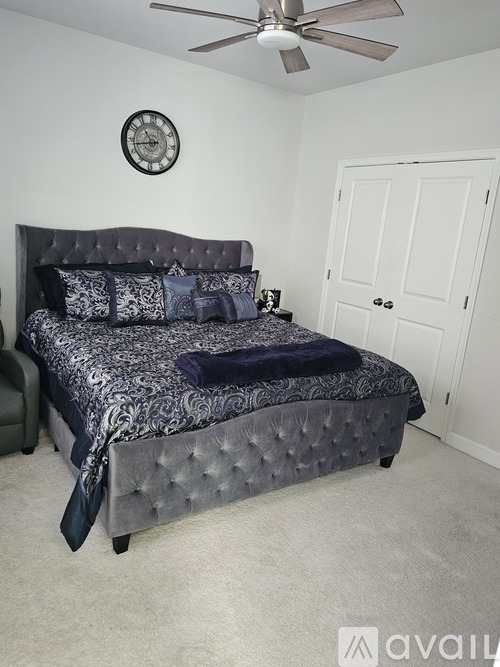 A bedroom with a bed, a ceiling fan, and a clock on the wall.