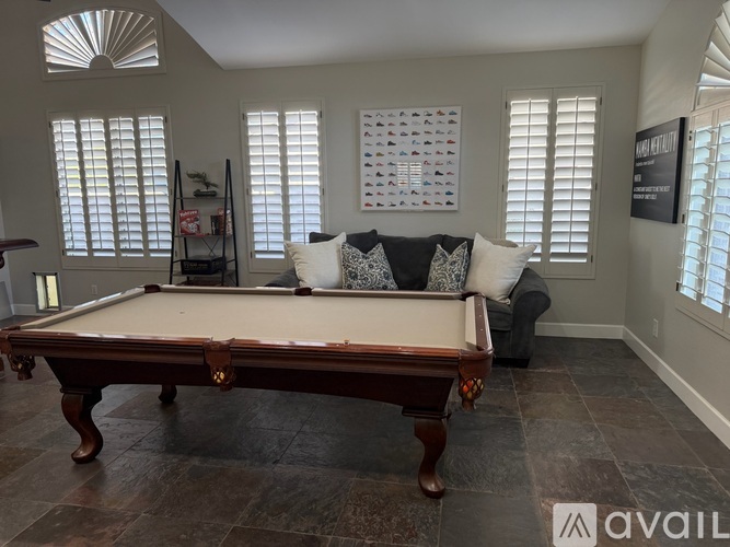 A pool table in a room with a couch and a calendar on the wall.