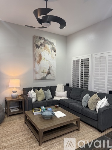 A living room with a grey couch, a wooden coffee table, and a large abstract painting on the wall.