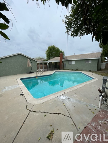 A pool surrounded by a concrete patio and a house.