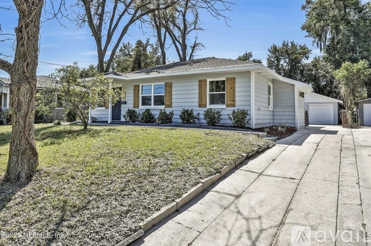 A house with a white exterior and a brown roof is surrounded by a well-maintained lawn and trees.