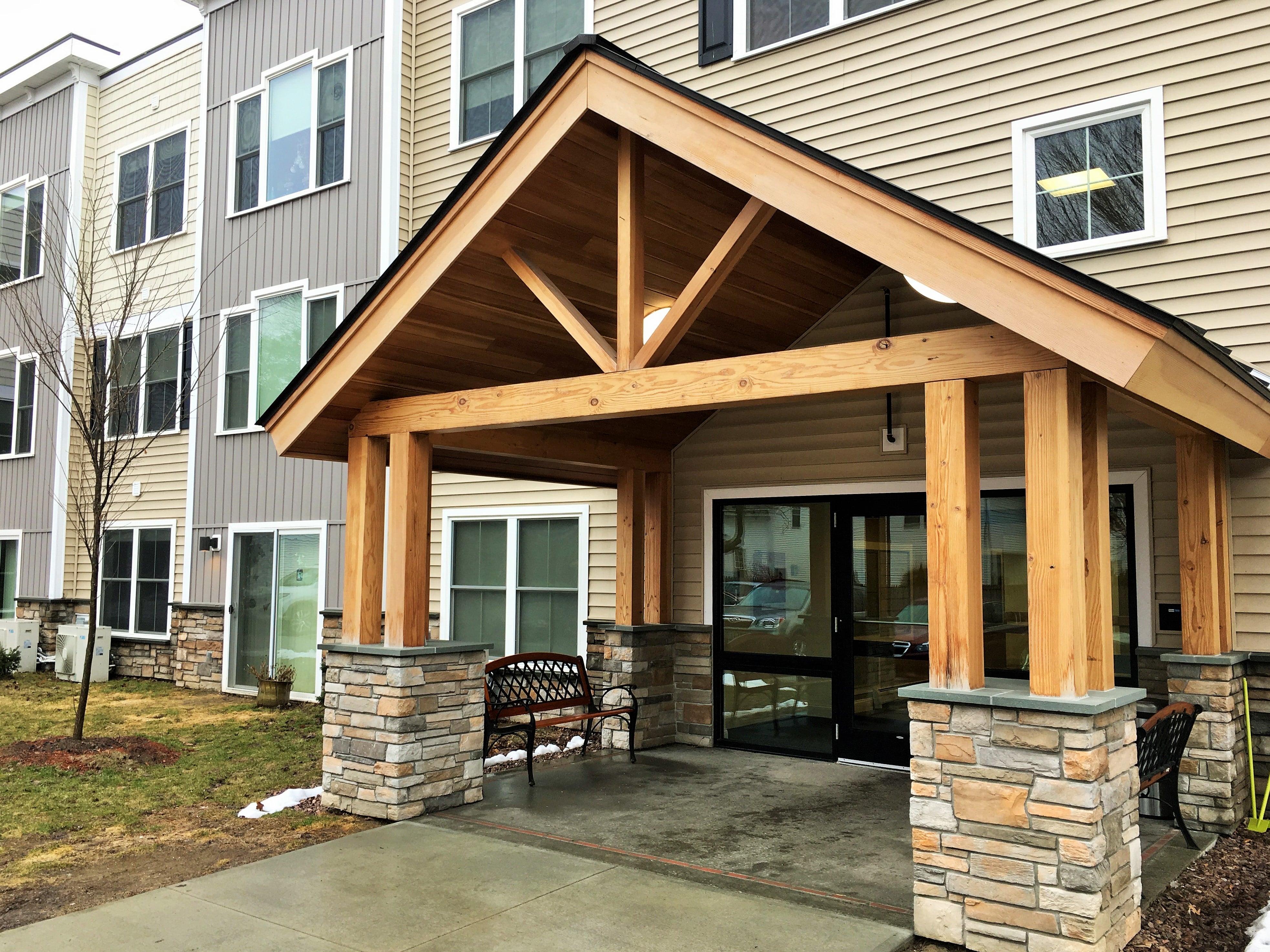 A wooden covered patio with a bench in front of a building.