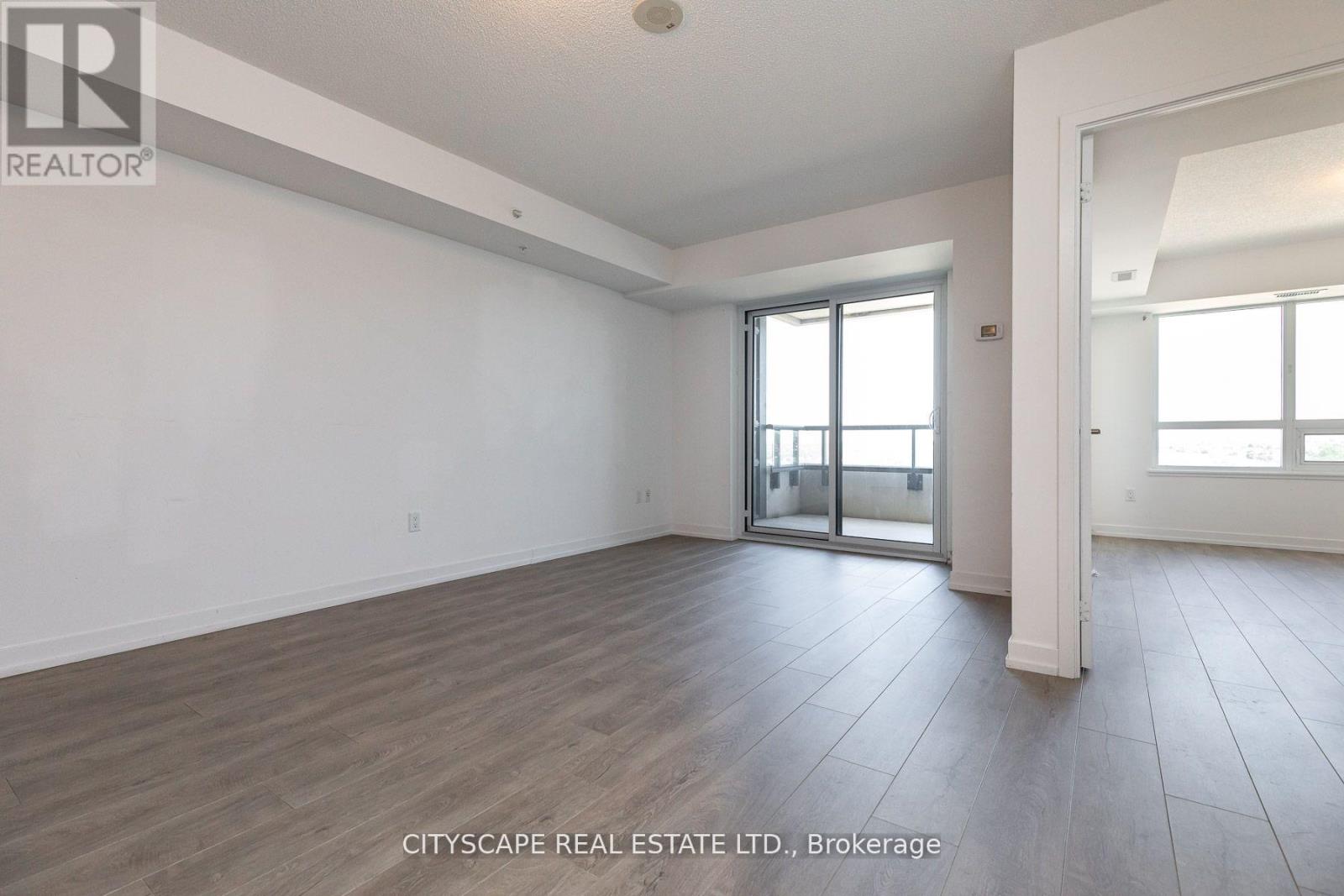 A spacious room with wooden flooring and a sliding glass door leading to another room.