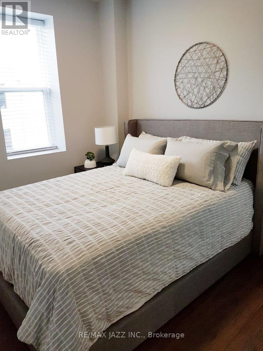 A bed with a white and grey striped comforter and pillows in a room with a round wall hanging and a small table with a lamp.