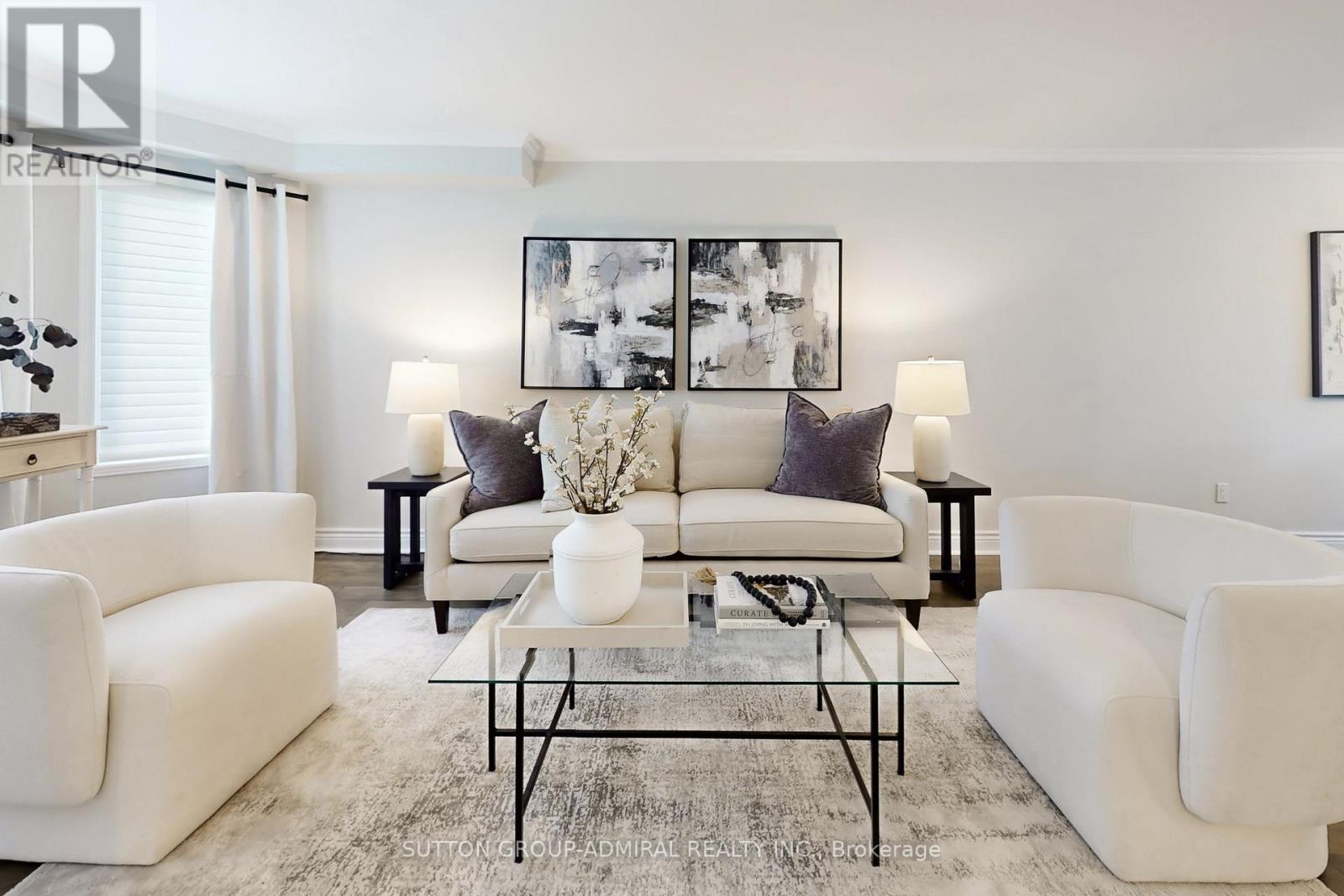 A living room with white furniture and a large painting on the wall.