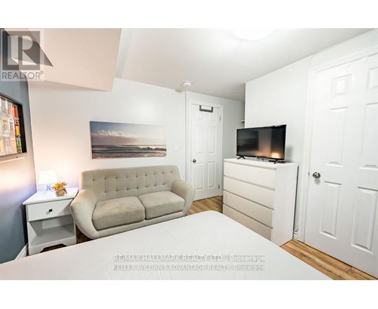 A well-lit bedroom with a beige sofa, a bed, and a television.