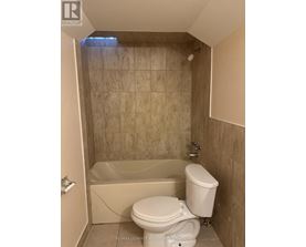 A white toilet is in a bathroom with a tiled shower area.