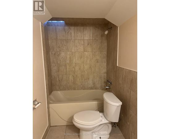 A white toilet is in a bathroom with a tiled shower area.