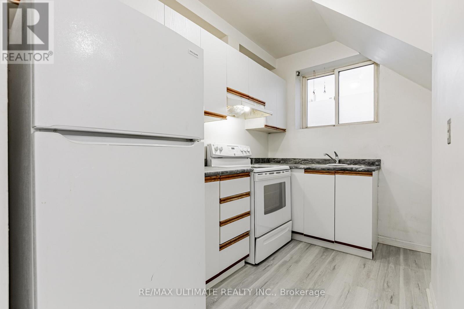 A white refrigerator is in a kitchen with white cabinets and a window.