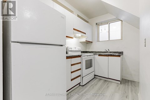 A white refrigerator is in a kitchen with white cabinets and a window.