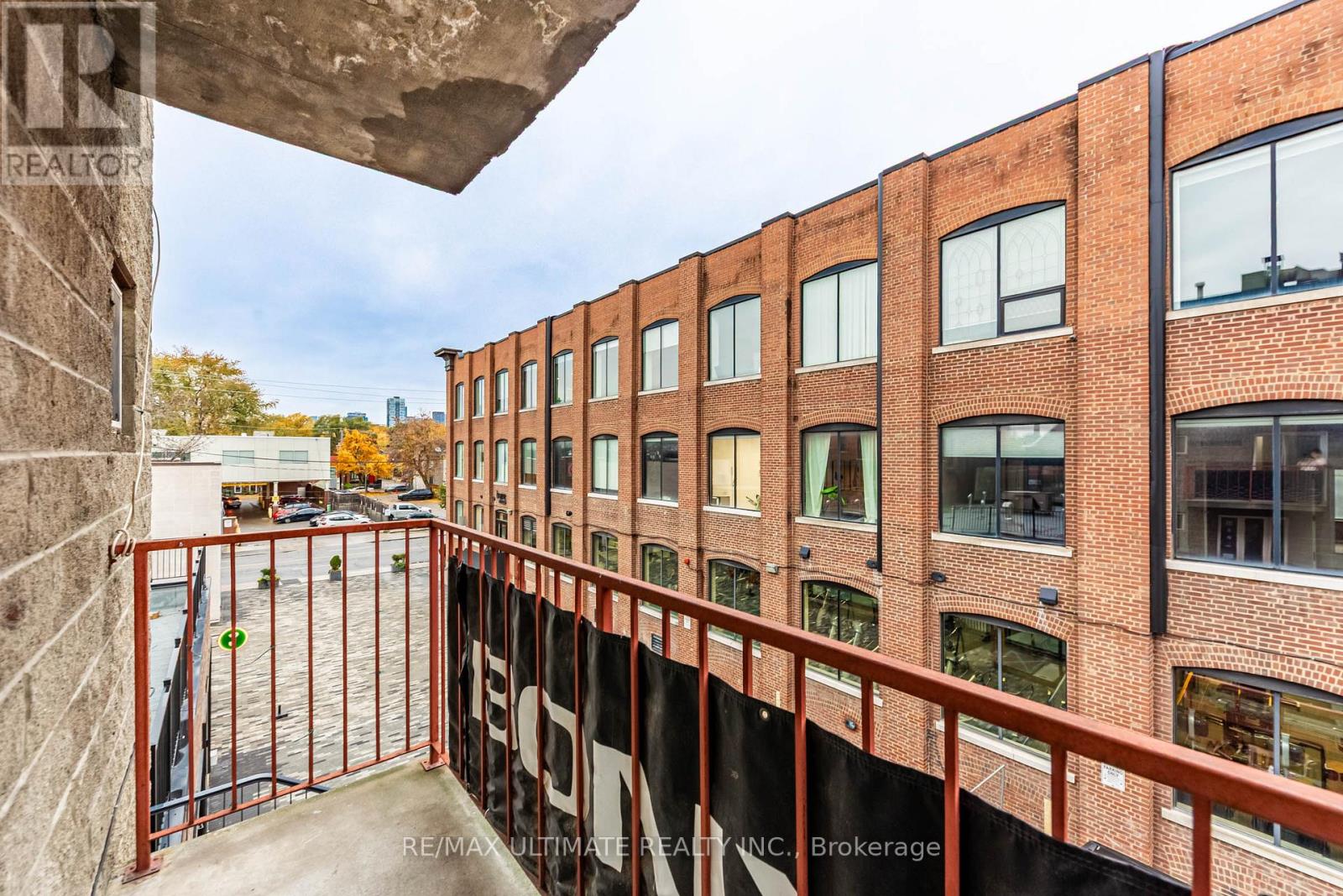 A balcony with a metal railing and a brick building in the background.