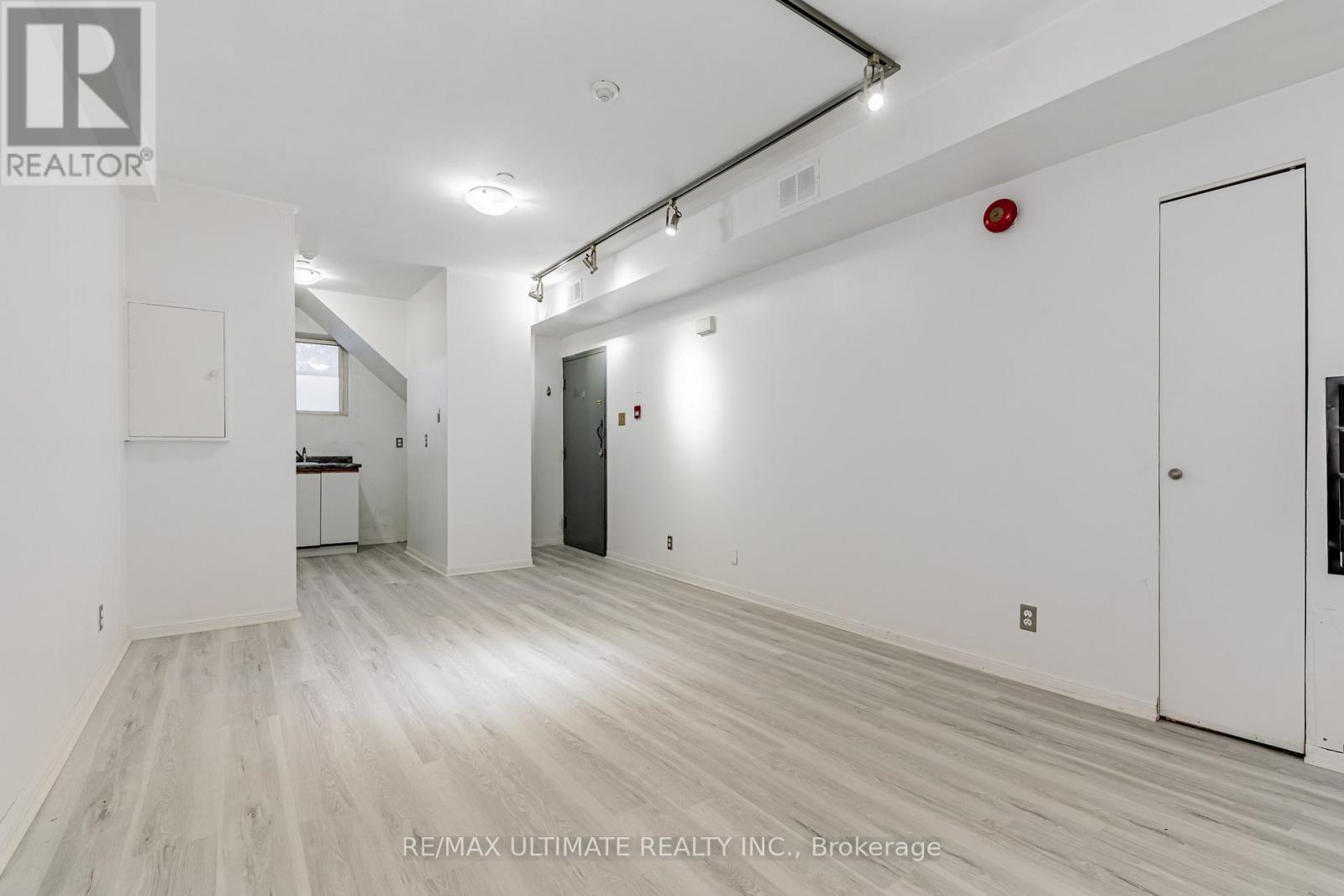 A spacious room with white walls and wooden flooring, featuring a white door and a black door.