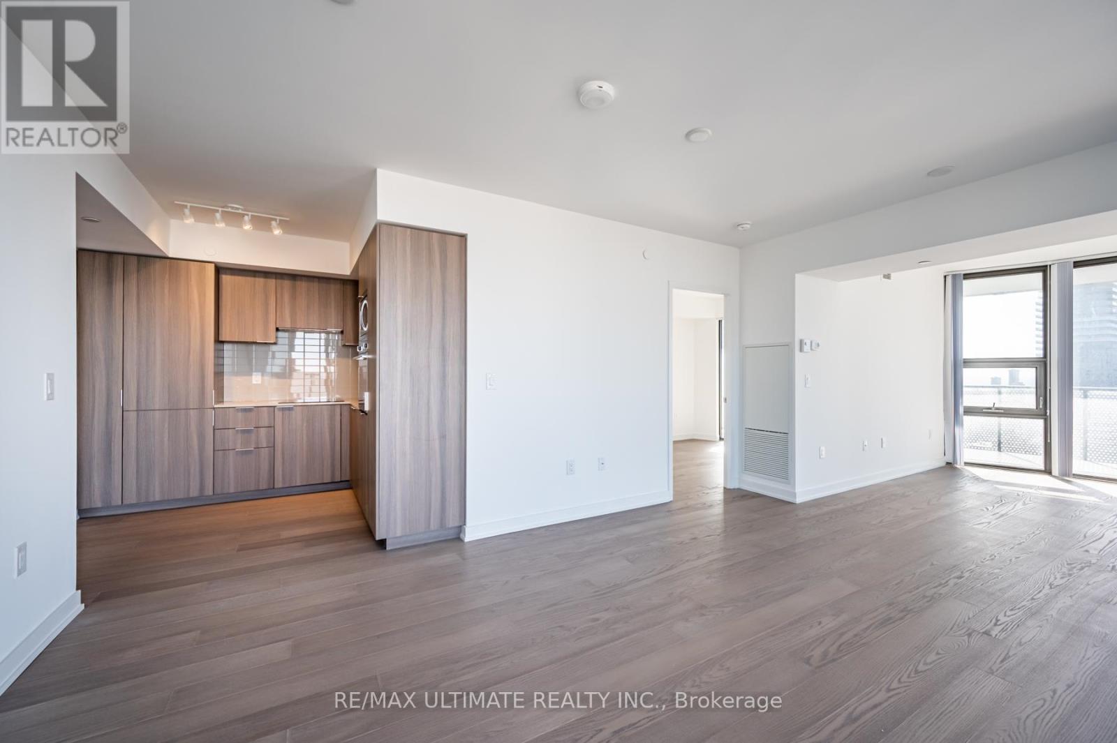 A spacious room with wooden flooring and a large window with curtains.