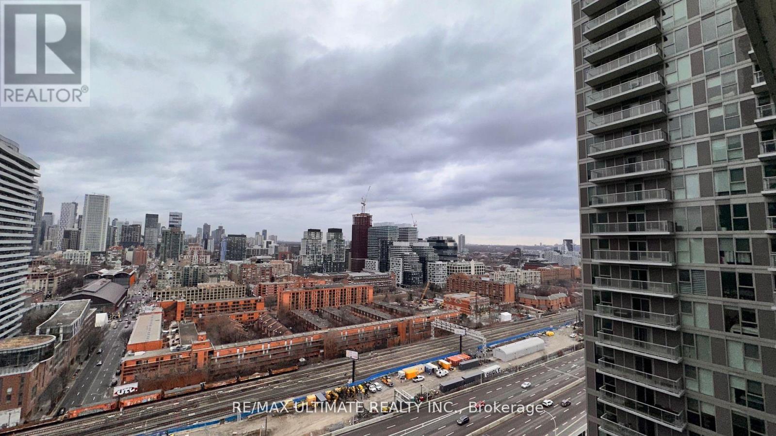 A cityscape with a tall building on the right and a train on the tracks in the middle.