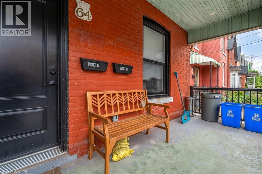 A wooden bench with a yellow cushion sits in front of a red brick building with a black door.