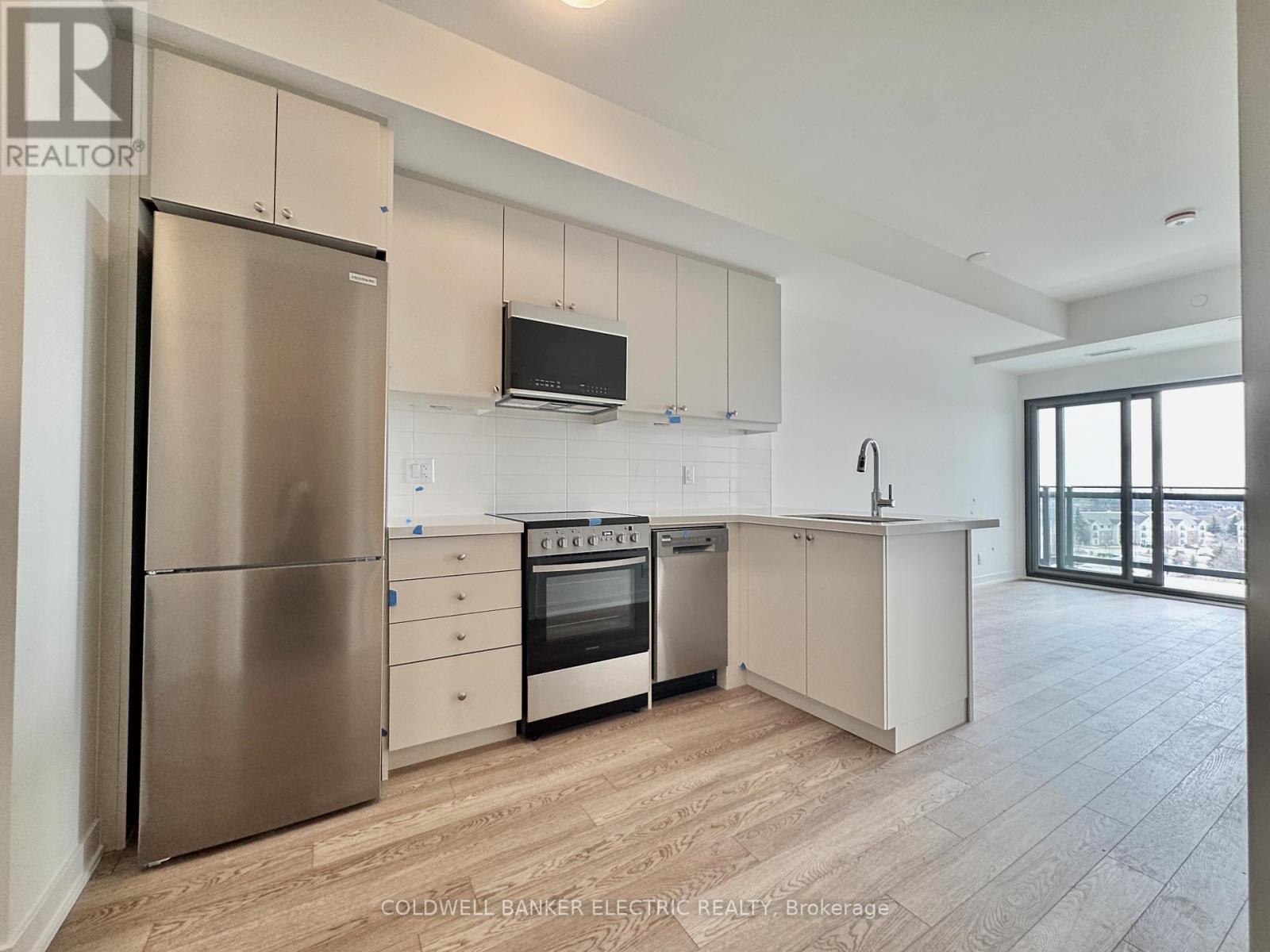 A modern kitchen with a stainless steel refrigerator and a flat screen TV mounted above the cabinets.