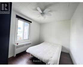 A bedroom with a bed, a window with a white curtain, a white ceiling fan, and a white radiator.