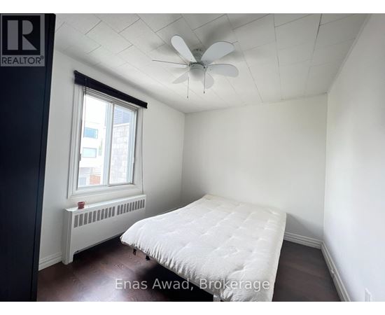 A bedroom with a bed, a window with a white curtain, a white ceiling fan, and a white radiator.