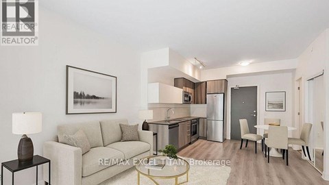 A well-lit, modern living room with a grey sofa, a dining table set for four, and a kitchen area in the background.