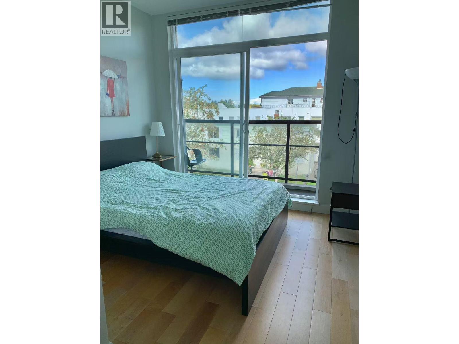 A bedroom with a bed, a nightstand, and a window overlooking a house.
