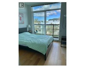 A bedroom with a bed, a nightstand, and a window overlooking a house.
