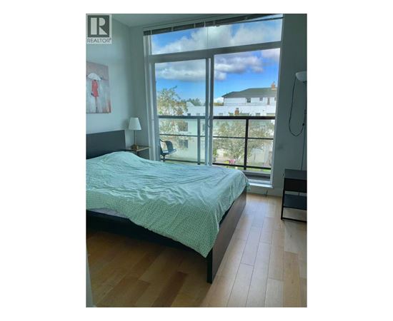 A bedroom with a bed, a nightstand, and a window overlooking a house.