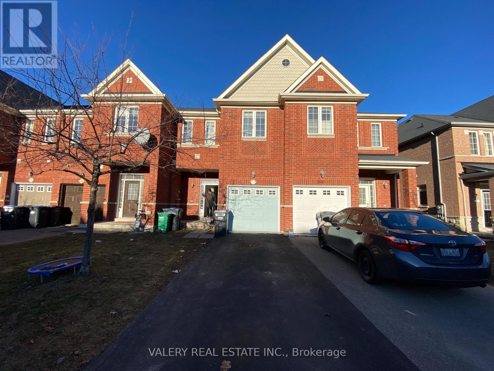 A car is parked in front of a brick house.