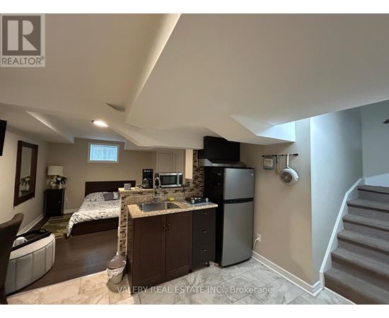 A kitchen area with a sink, refrigerator, and a bedroom with a bed and a window.