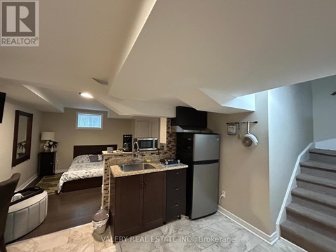 A kitchen area with a sink, refrigerator, and a bedroom with a bed and a window.