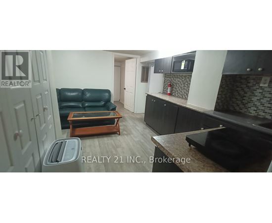 A black leather sofa sits in a kitchen with a wooden coffee table in front of it.